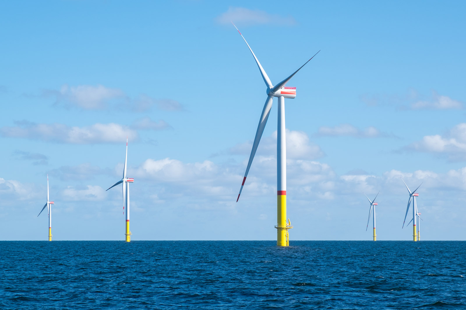 A clear sky over a group of offshore wind turbines with colourful bases, standing in the blue sea.
