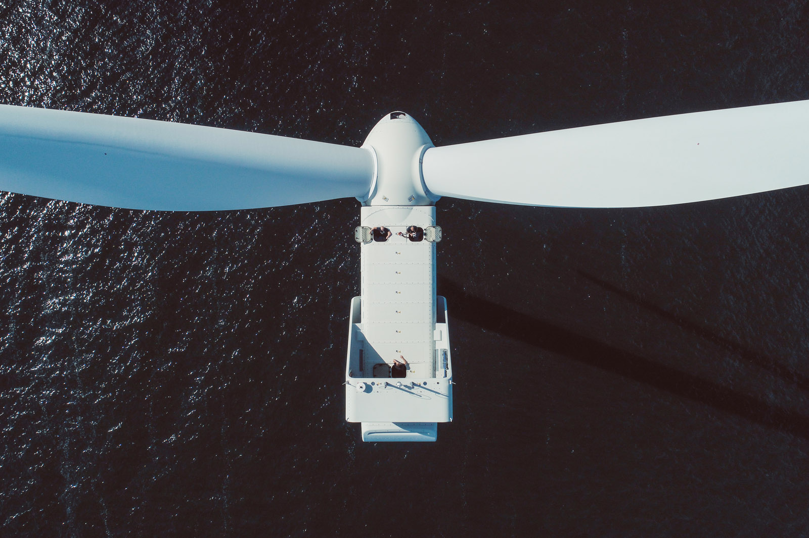 Aerial view of a white wind turbine rotor above dark, shimmering water, with detailed components visible.