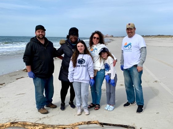 A group of volunteers stands on a beach, wearing gloves and t-shirts, promoting community cleanup efforts.