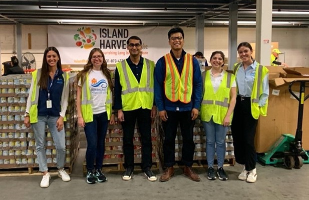 A group of volunteers in safety vests pose in front of shelves filled with canned goods at Island Harvest.