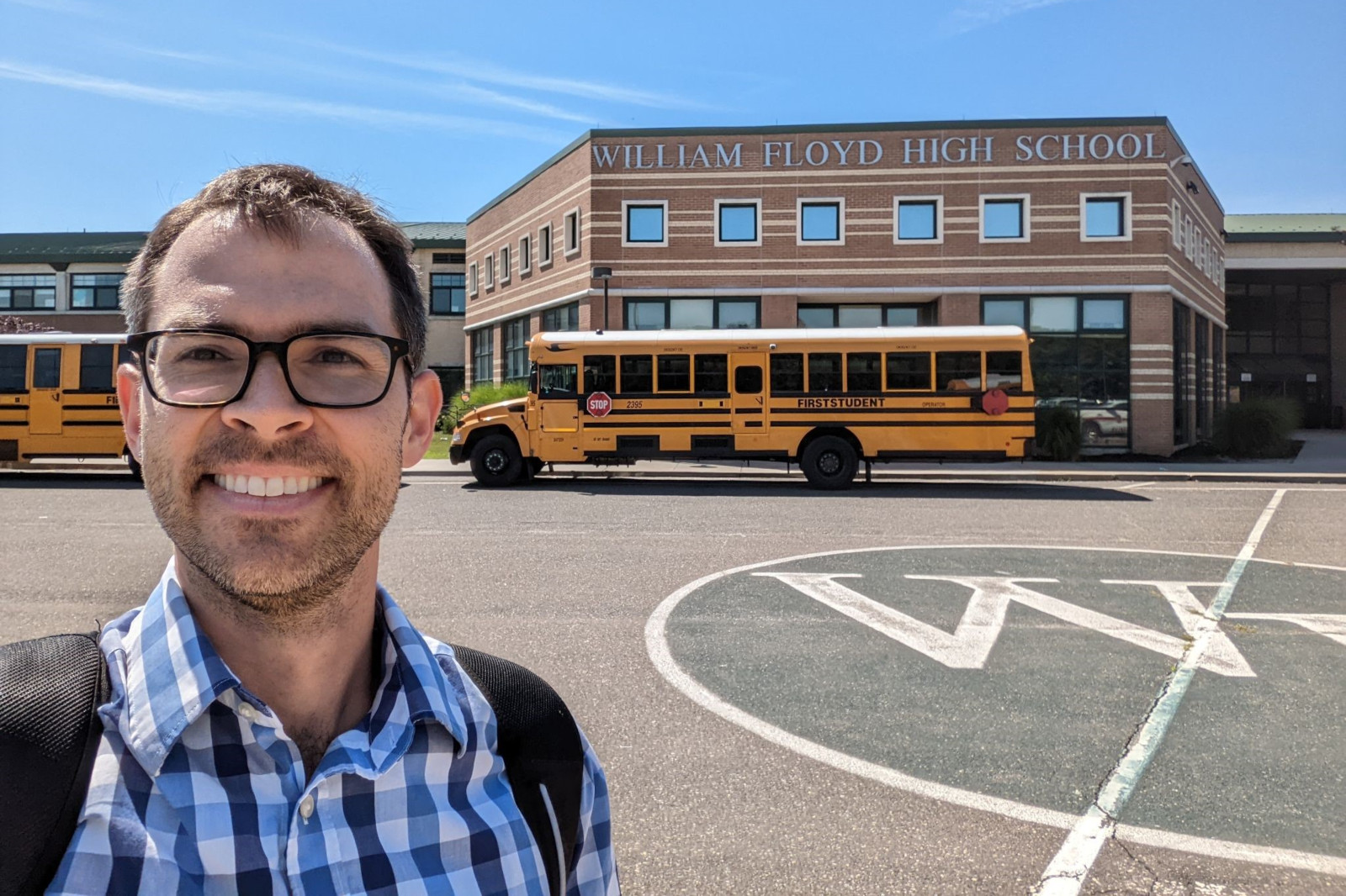 A person stands in front of William Floyd High School, with yellow school buses parked nearby.
