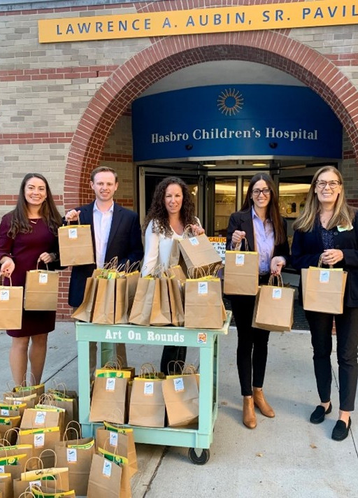 A group stands outside Hasbro Children's Hospital with bags for donation on a cart labelled 'Art On Rounds'.