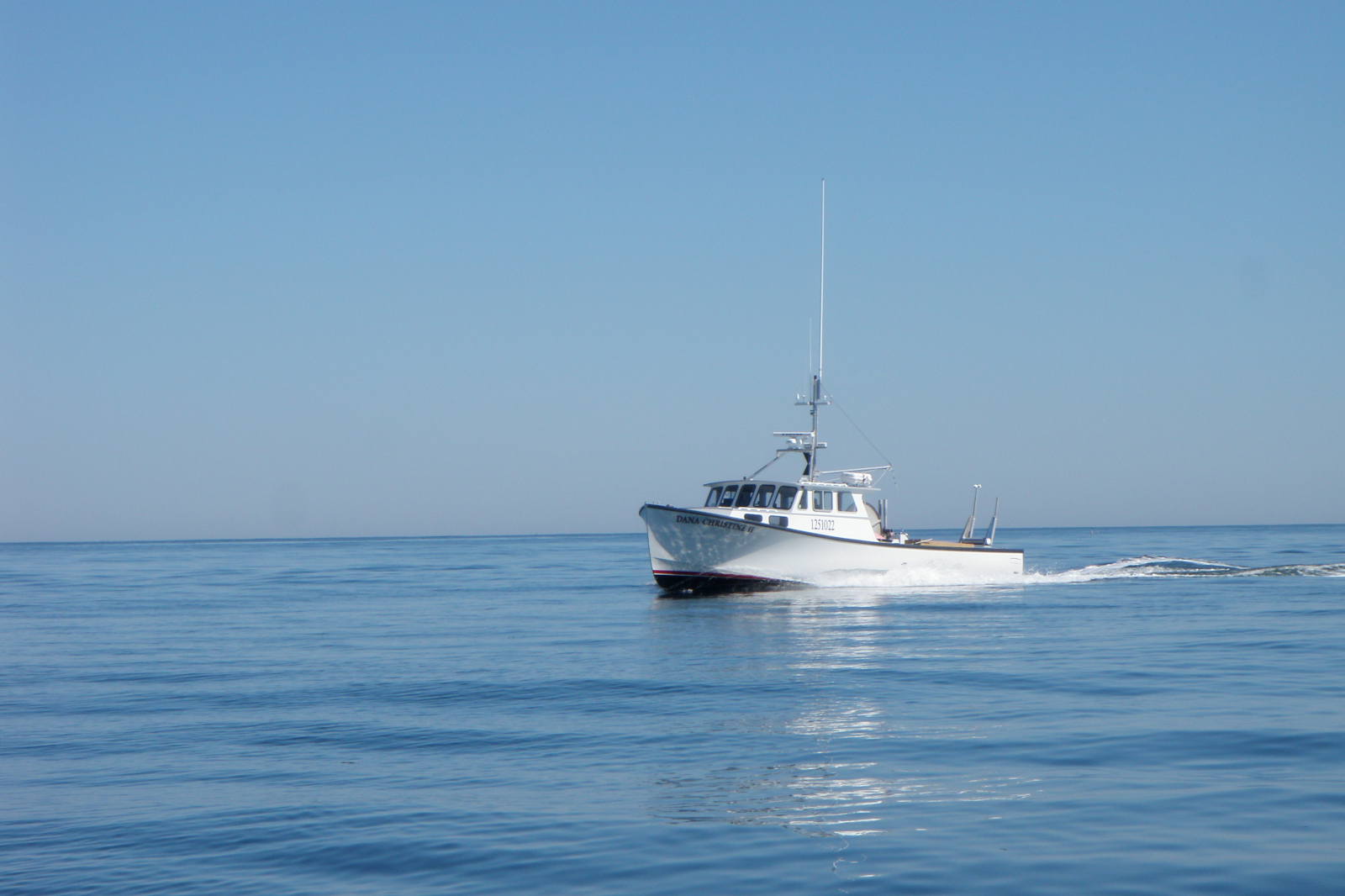A white fishing boat named 'DANA CYRUS' navigating through calm blue waters under a clear blue sky.