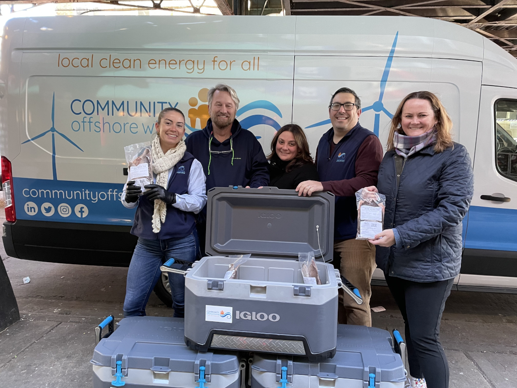 A group of people stands in front of a van promoting local clean energy. They hold packages and boxes labelled IGLOO.