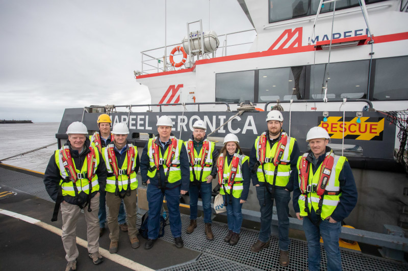 A group of individuals in safety vests and helmets stand on a boat named 'Mareel Veronica'.