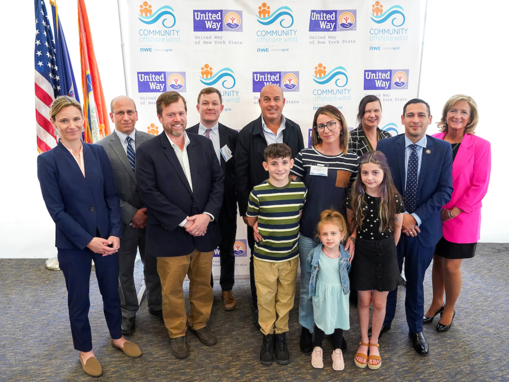 A diverse group of adults and children posing together at an event with United Way branding in the background.