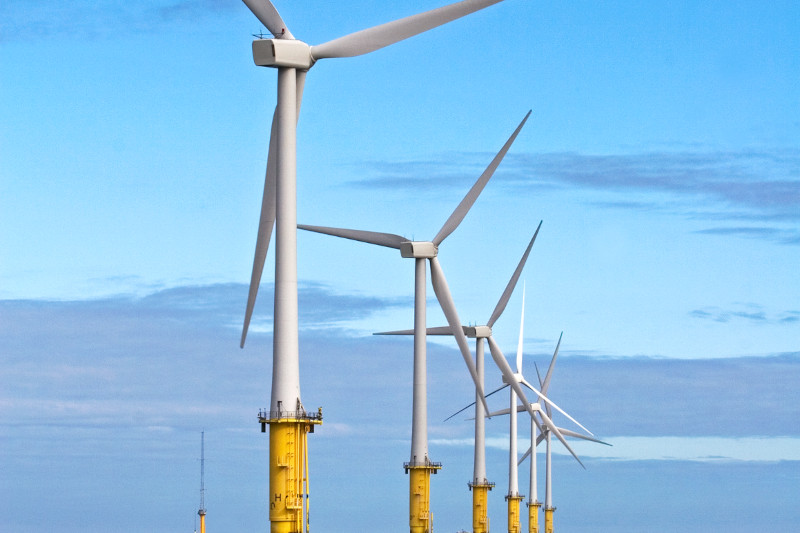 A row of tall wind turbines on yellow bases against a blue sky with clouds.