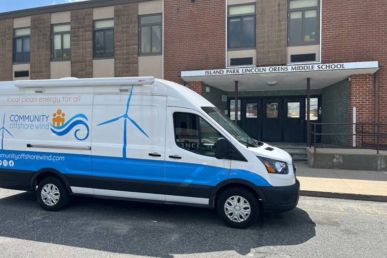 A white van with a blue stripe parked outside Island Park Lincoln Orens Middle School, promoting local clean energy.