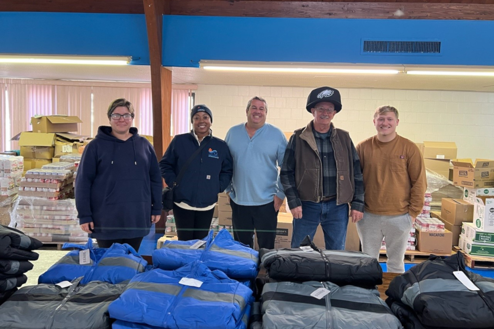 A group of five people stands in front of stacks of boxes with clothing items on the table.
